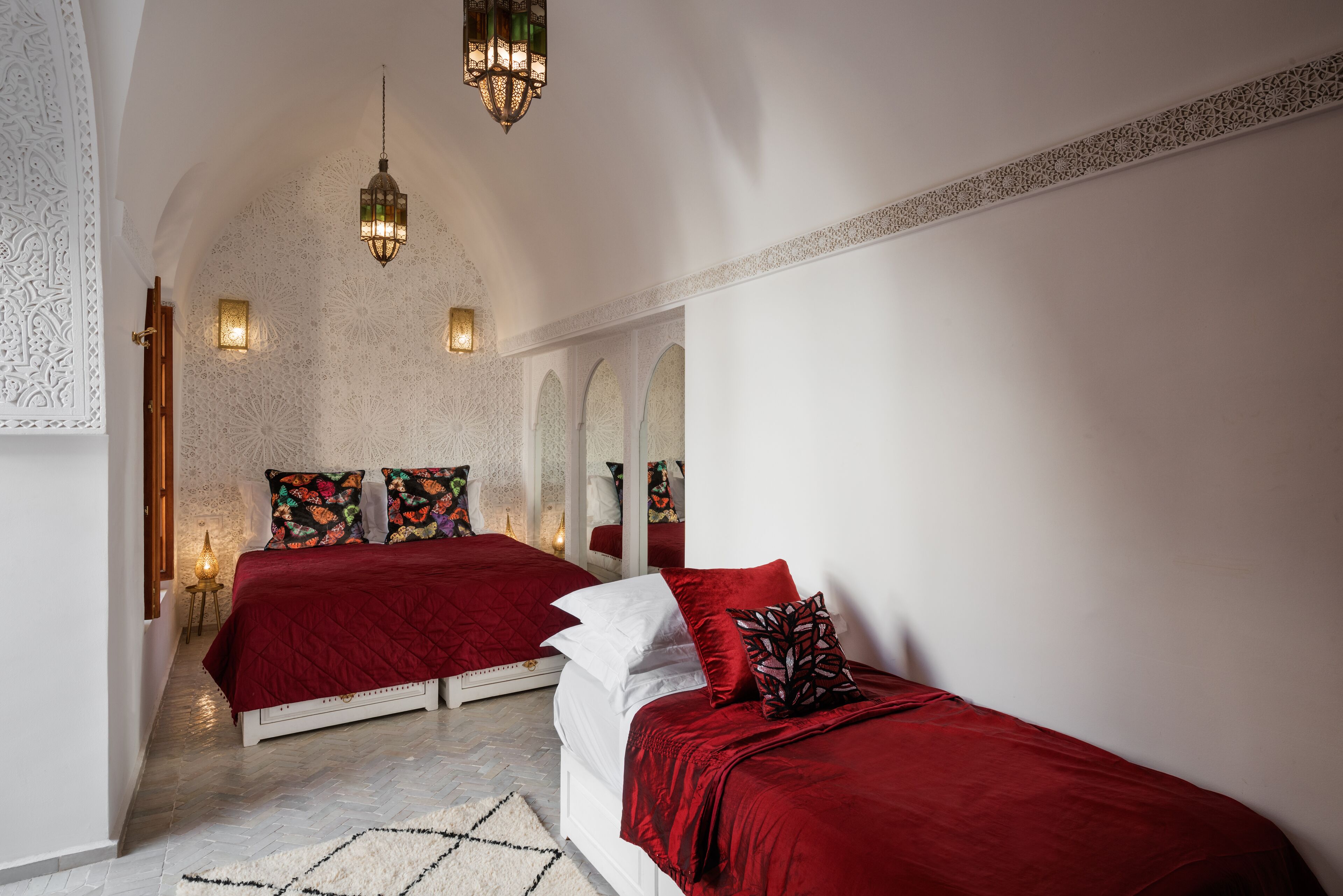 A bedroom with two beds, ornate wall designs, and hanging lamps.