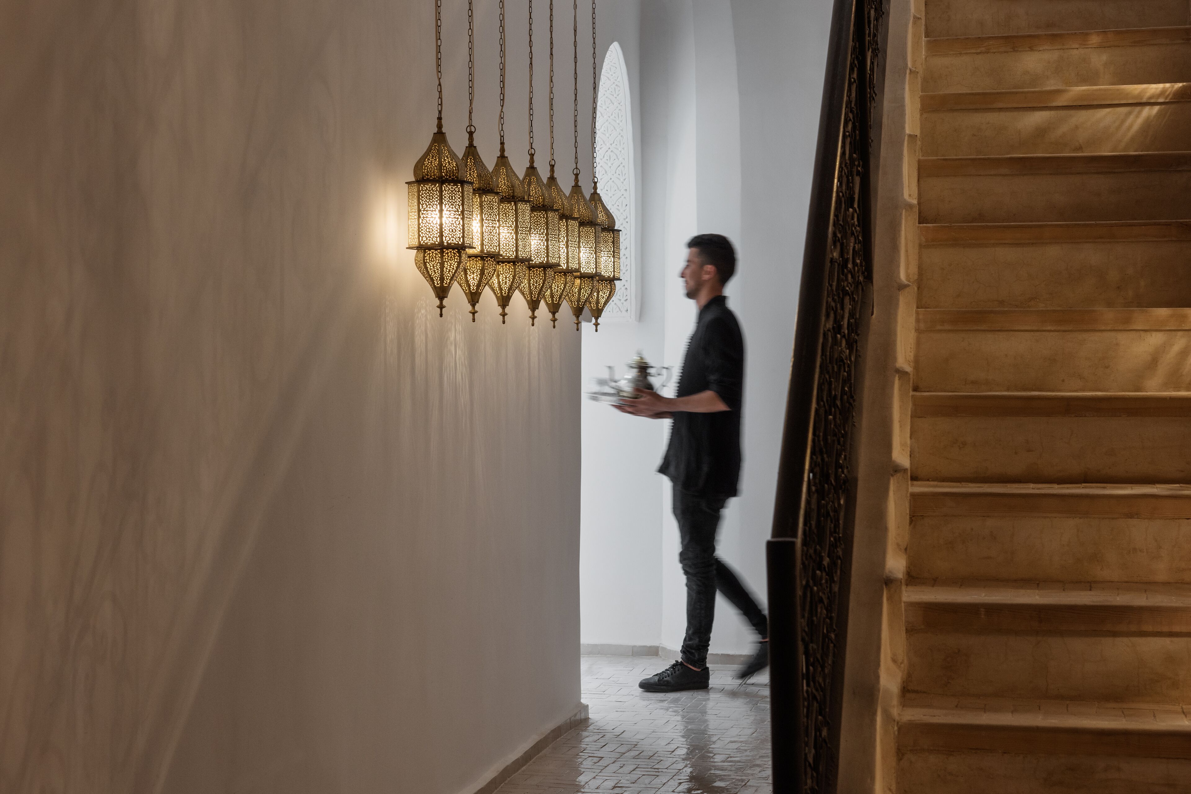A person walking through a hallway with a patterned wall and a hanging light fixture.