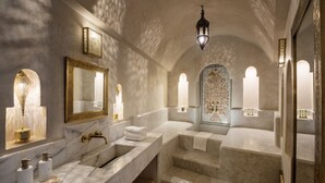 Un baño lujoso con encimeras de mármol, un espejo grande, apliques de pared ornamentados y una pared decorada con azulejos.