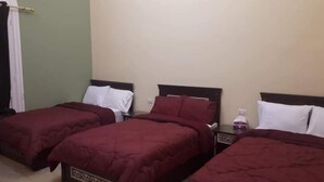 A hotel room with three single beds, each with a dark headboard and white pillows. The room has a green wall and a wooden floor. - Cairo (Cairo)