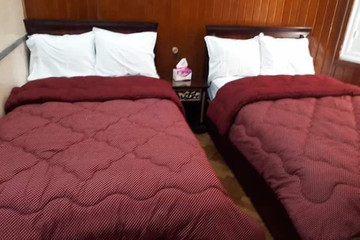 A double bed with a red quilted bedspread and white pillows, positioned against a wooden headboard.