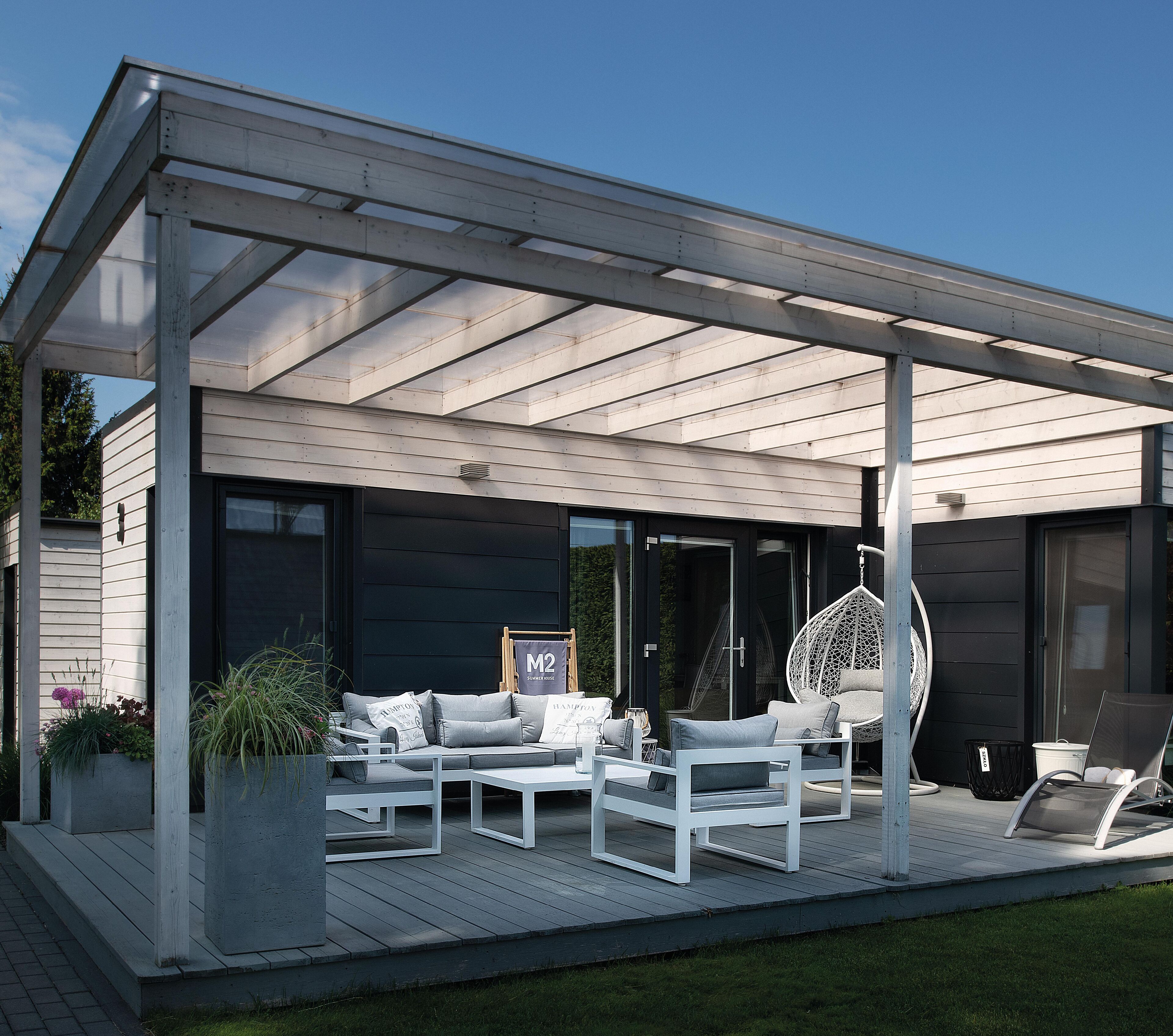 Un área de estar al aire libre cubierta con un diseño moderno, que incluye una pérgola, una silla colgante y un conjunto de sofás.