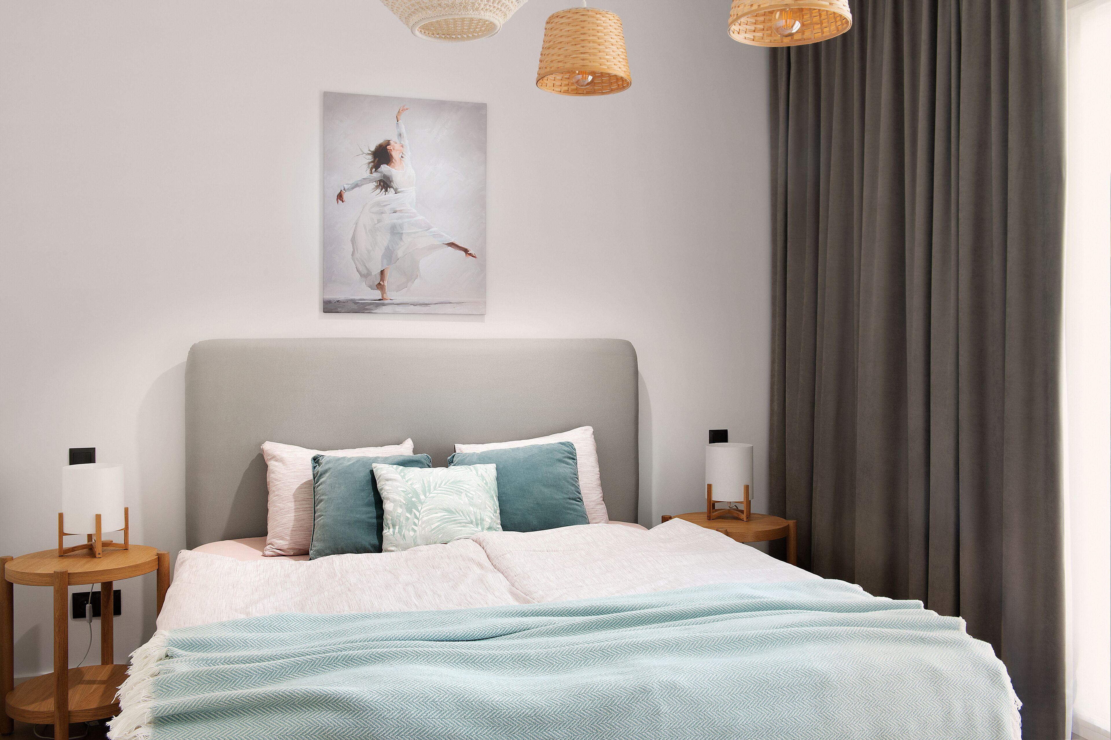 Un dormitorio con cama, almohadas, una mesita de noche, una lámpara y un cuadro en la pared.