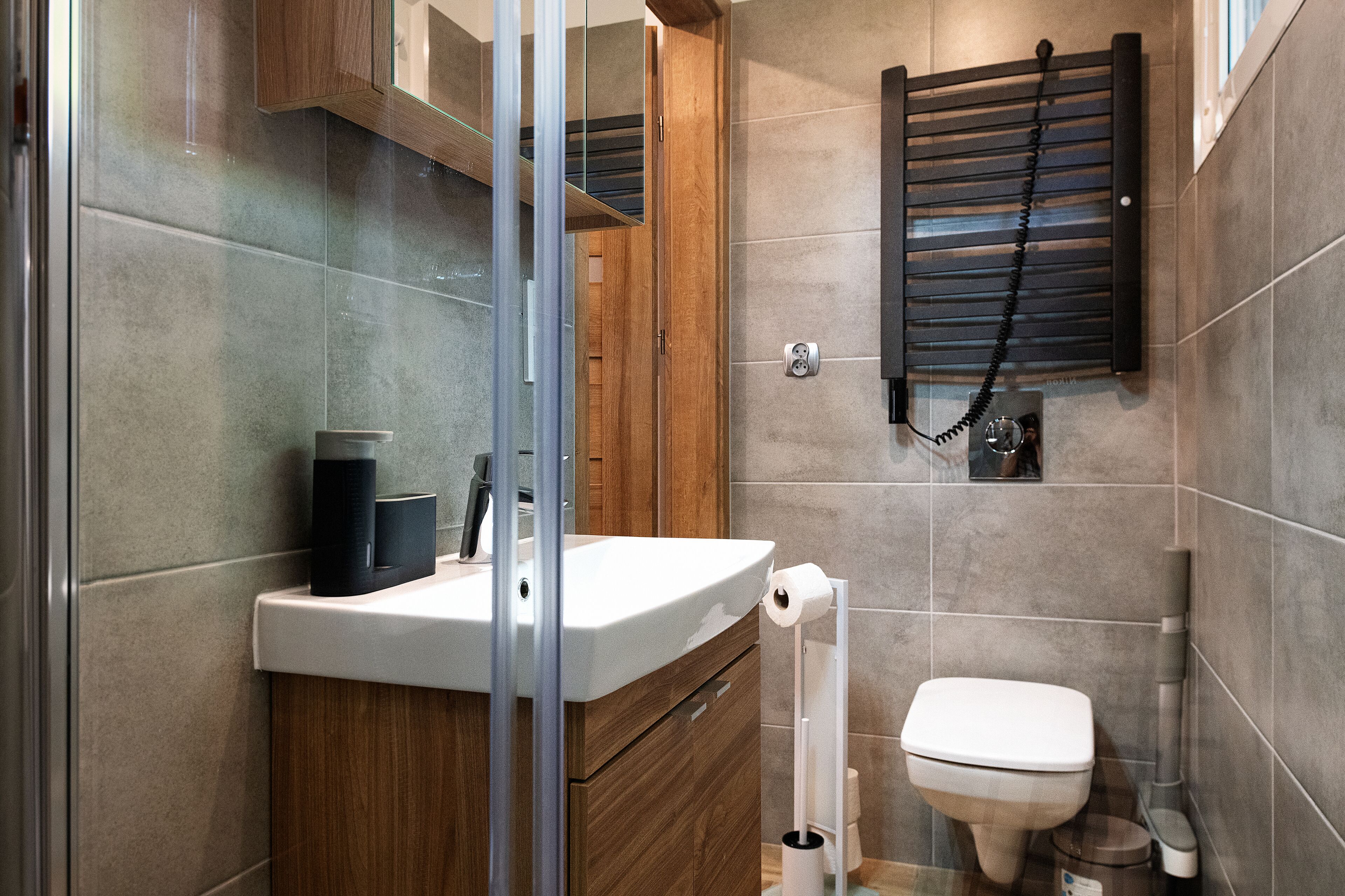 Un baño moderno con cabina de ducha de vidrio, tocador de madera, inodoro y toallero.