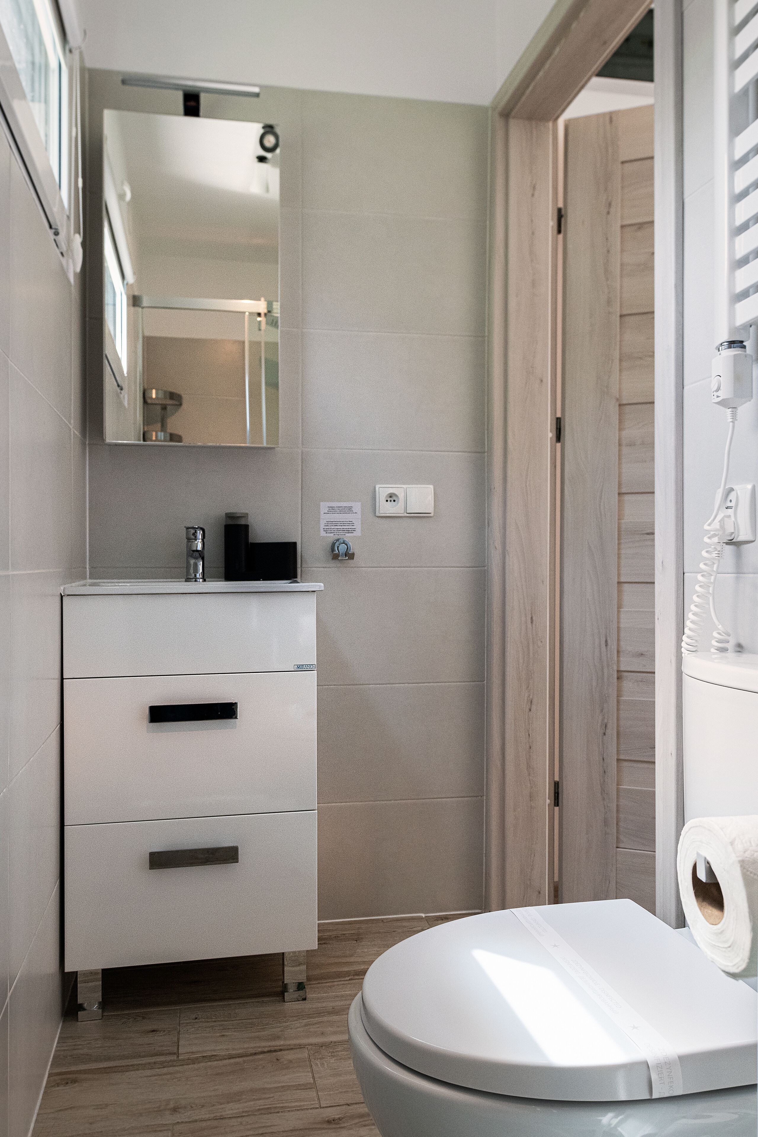 Ein modernes Badezimmer mit einer weißen Toilette, einem Waschbecken mit Spiegel darüber und einer Holztür.