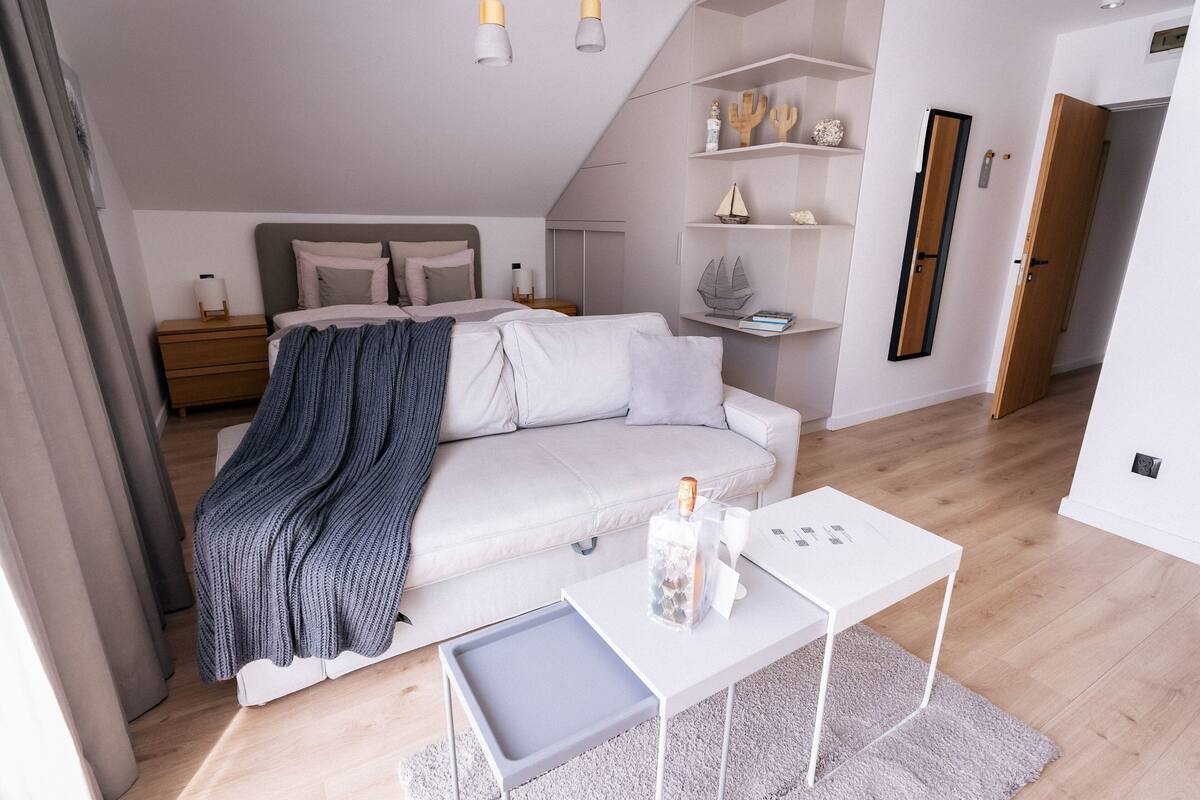 Une chambre moderne avec un lit, des tables de chevet, un canapé blanc, une petite table blanche et un plancher en bois.