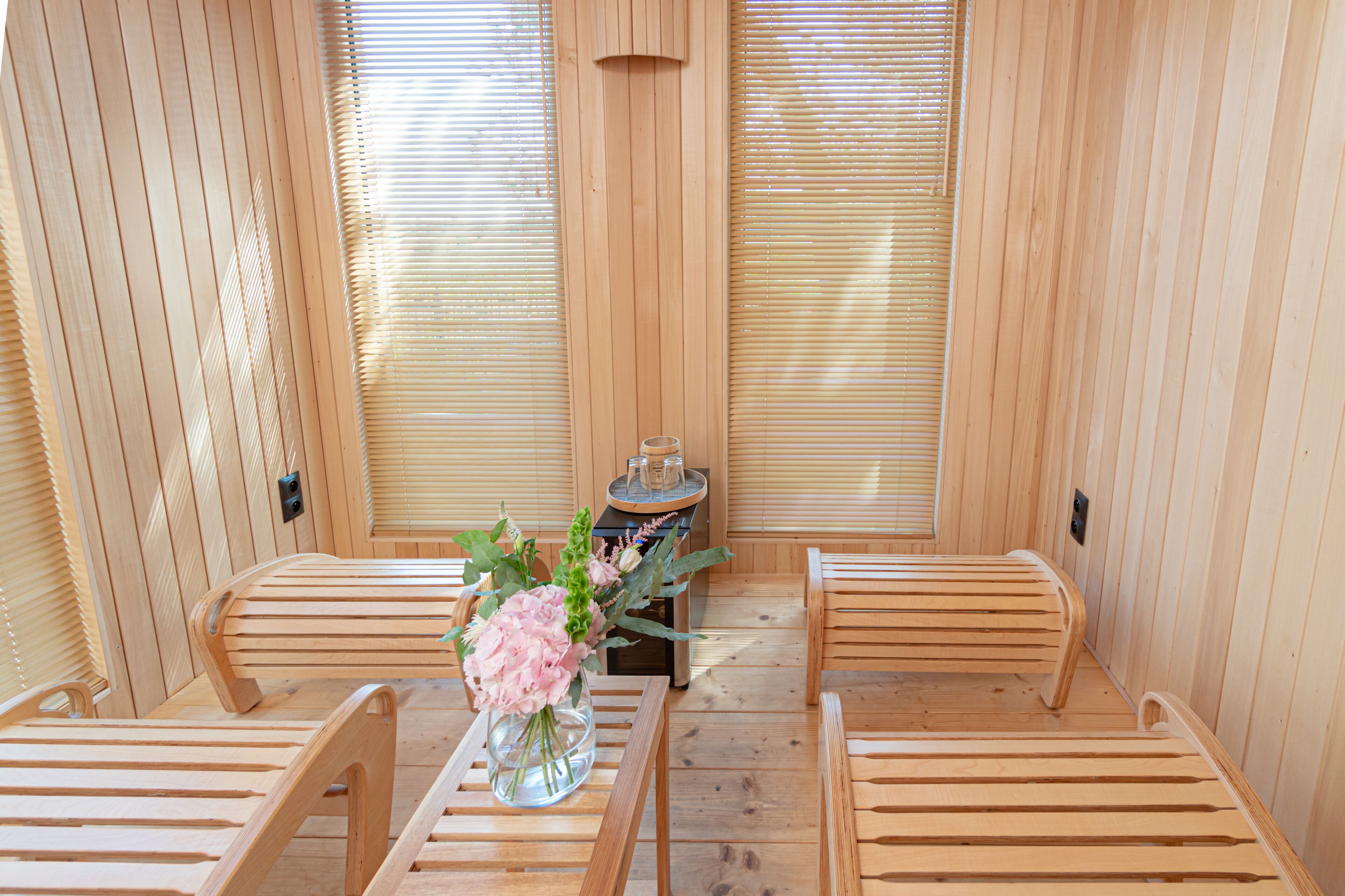 Un sauna en bois, avec des bancs et une table agrémentée d’un vase de fleurs.