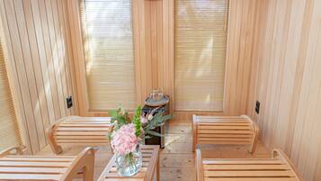 Un sauna en bois, avec des bancs et une table agrémentée d’un vase de fleurs.