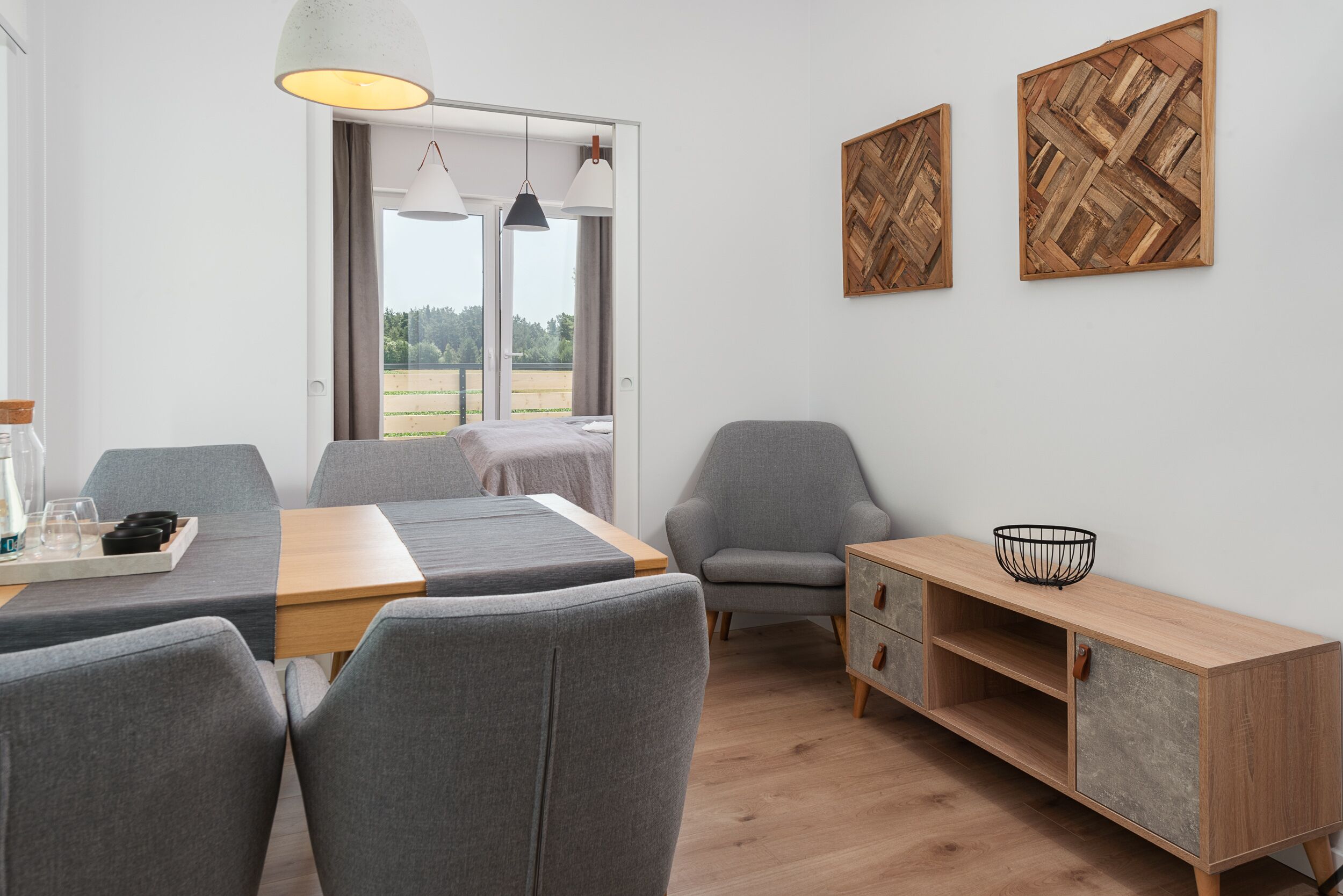 Una habitación moderna con una mesa de comedor, sillas grises, un armario de madera y dos obras de arte en la pared.