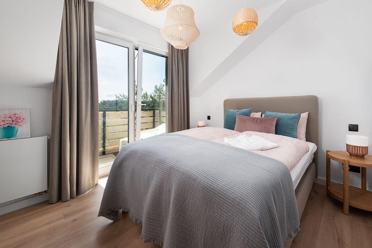 Une chambre avec un grand lit, une table de chevet, une fenêtre avec des rideaux et une vue sur l’extérieur.