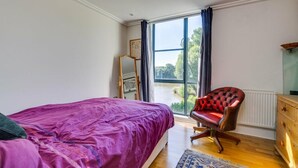 A bedroom with a bed, a chair, a dresser, and a window with a view of greenery. - Brand New 2-bed Apartment in Brentford Kew Gardens (Brentford)