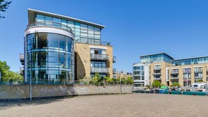 A modern building with a curved glass facade, a flat roof, and a brick base. - Brand New 2-bed Apartment in Brentford Kew Gardens (Brentford)