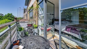 A balcony with a glass door, a round table, and potted plants. - Brand New 2-bed Apartment in Brentford Kew Gardens (Brentford)