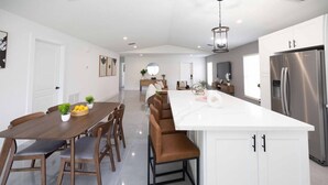 Una cocina moderna con una isla grande, armarios blancos y electrodomésticos de acero inoxidable.