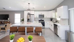 Una cocina moderna con armarios blancos, electrodomésticos de acero inoxidable y una isla central con asientos.