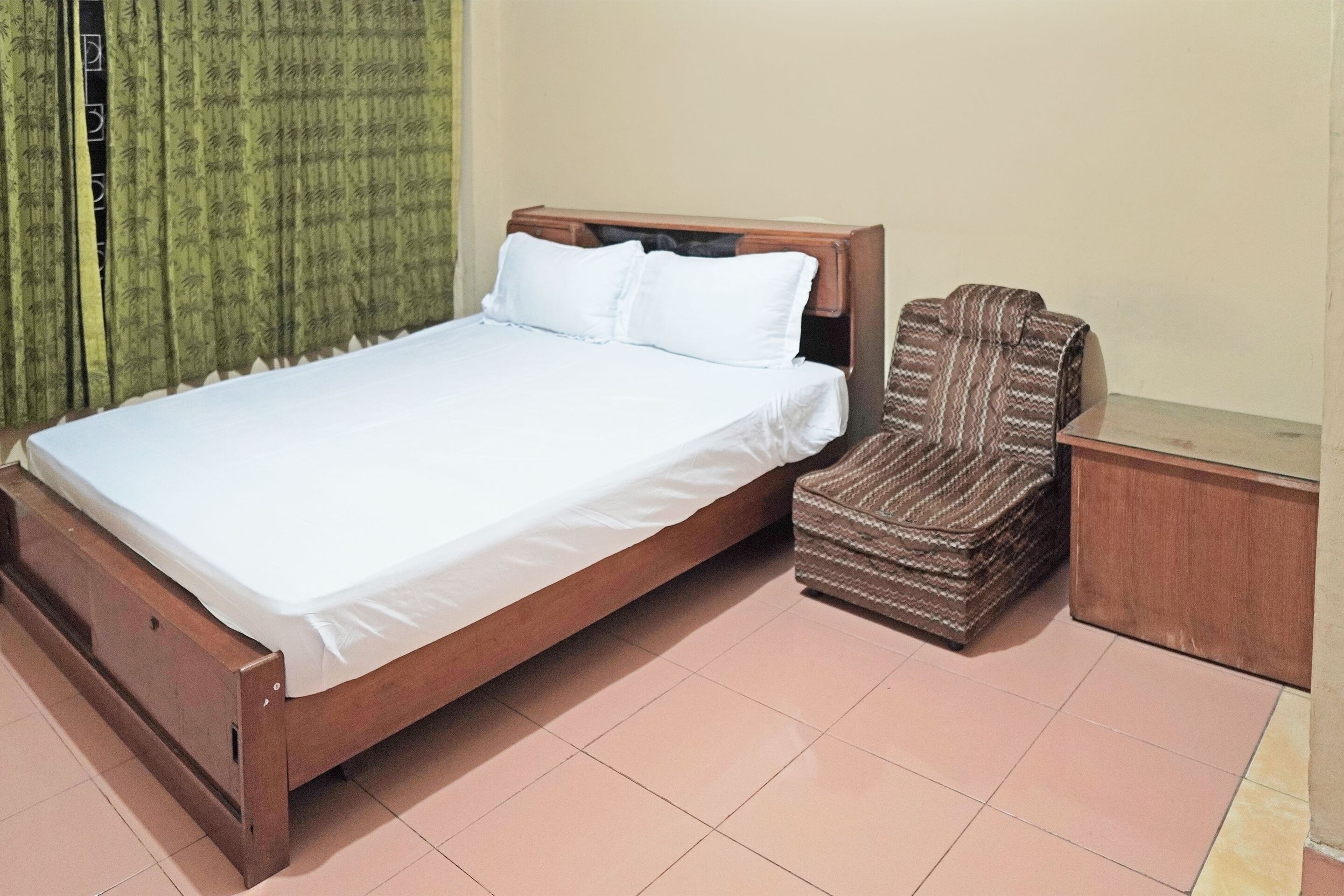 A single bed with a wooden frame and white bedding, a striped armchair, and a small wooden nightstand.