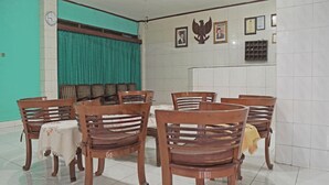 A dining area with wooden chairs and a table, a clock on the wall, and framed pictures. - Capital O 92958 Hotel Raflessia Syariah (Lawang Kidul)