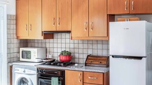 A compact kitchen with wooden cabinets, a microwave, a stove, a washing machine, and a refrigerator. - Villa Chara Mari (Neo Chorio)