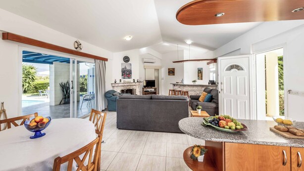 A spacious living area with a dining table, sofas, and a kitchen counter with fruit. - Villa Chara Mari (Neo Chorio)