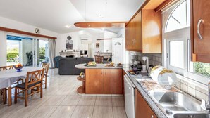 A modern kitchen with wooden cabinets, a granite countertop, and a built-in dishwasher. - Villa Chara Mari (Neo Chorio)