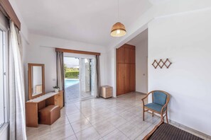 A spacious room with a wooden vanity, a chair, and a view of a swimming pool through a glass door. - Villa Chara Mari (Neo Chorio)