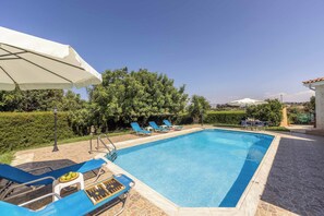 A swimming pool with blue water, surrounded by blue lounge chairs and a white umbrella. - Villa Chara Mari (Neo Chorio)