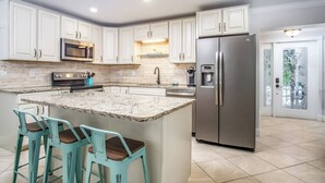 A kitchen with white cabinets, a stainless steel refrigerator, a granite island with bar stools, and a microwave. - Happy Tingler With Pool Tiki and 100 ft of Dockage Right Next to Sombrero Beach (Marathon)