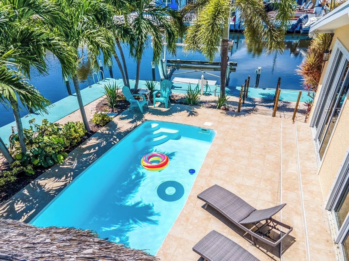 Une piscine avec des chaises longues, des palmiers et un quai pour bateaux.