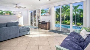 A spacious living room with a grey sofa, a blue couch, a wooden cabinet, and a television. - Happy Tingler With Pool Tiki and 100 ft of Dockage Right Next to Sombrero Beach (Marathon)