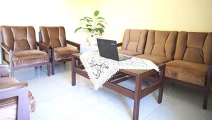 A living room with a brown sofa, two brown armchairs, a wooden coffee table with a laptop and a white lace table runner.
