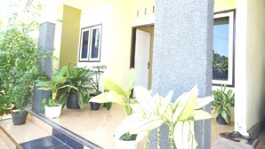 A covered outdoor area with potted plants, a tiled floor, and a door leading to an interior space.