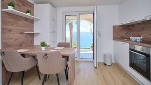 A modern kitchen with white cabinets, wooden accents, and a view of the sea through a glass door. - Bella Vista Dalmatien #1 (Celina)