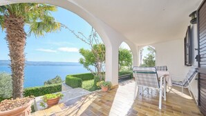 A covered patio with a view of the sea, a palm tree, and a seating area with a table and chairs. - Bella Vista Dalmatien #1 (Celina)