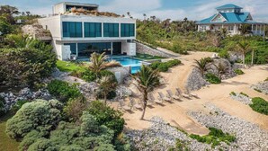 En moderne ejendom ved stranden med swimmingpool, et stort hus med blåt tag og en velplejet have.