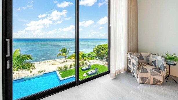 En moderne stue med en stor skydedør, der fører ud til en balkon med udsigt over strand og pool.