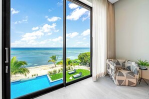 Una sala de estar moderna con un amplio ventanal corredero que da a un balcón con vistas a la playa y la piscina.