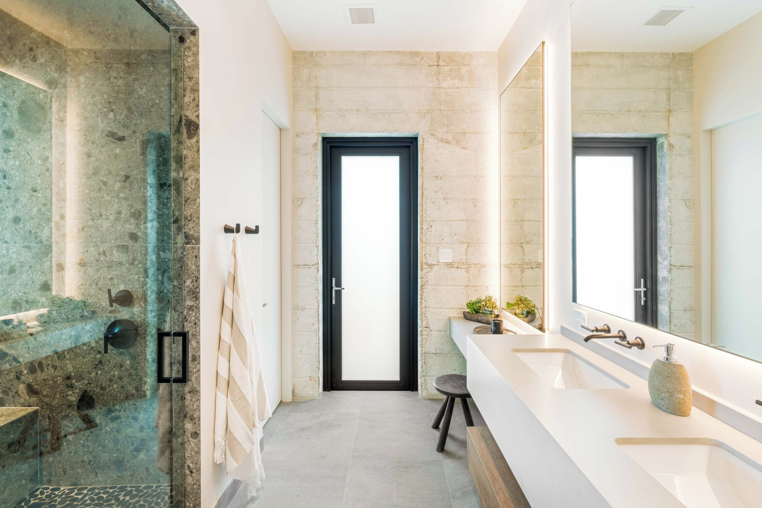 A modern bathroom with a large mirror, two sinks, and a shower area with a glass door.