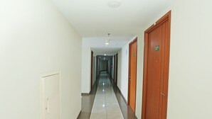 A long, narrow hallway with a tiled floor, white walls, and wooden doors on one side. - Capital O 92971 Pelangi Residence (South Tangerang)