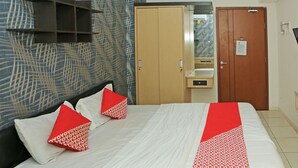A hotel room with a bed, two red pillows, a white bedspread, and a red and white patterned throw. There is a wooden wardrobe, a mirror, and a small table with a lamp. - Capital O 92971 Pelangi Residence (South Tangerang)
