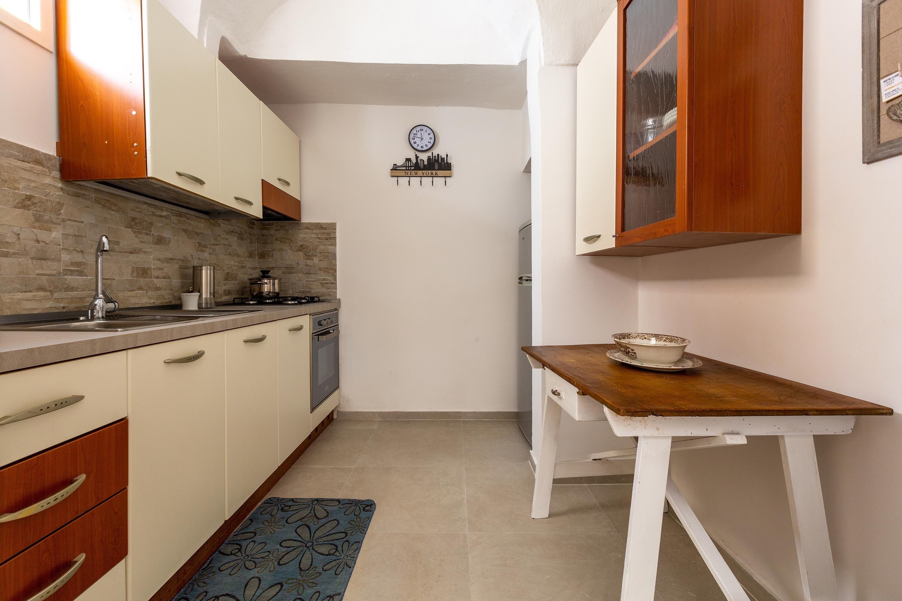 A compact kitchen with white cabinets, a wooden countertop, a small table, and a cityscape wall decoration.