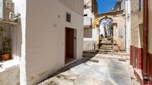 A narrow street with a white building on the left, a wooden door, and a stone staircase leading to a balcony. - 3482 Vico dei Mille by Barbarhouse (Tuglie)