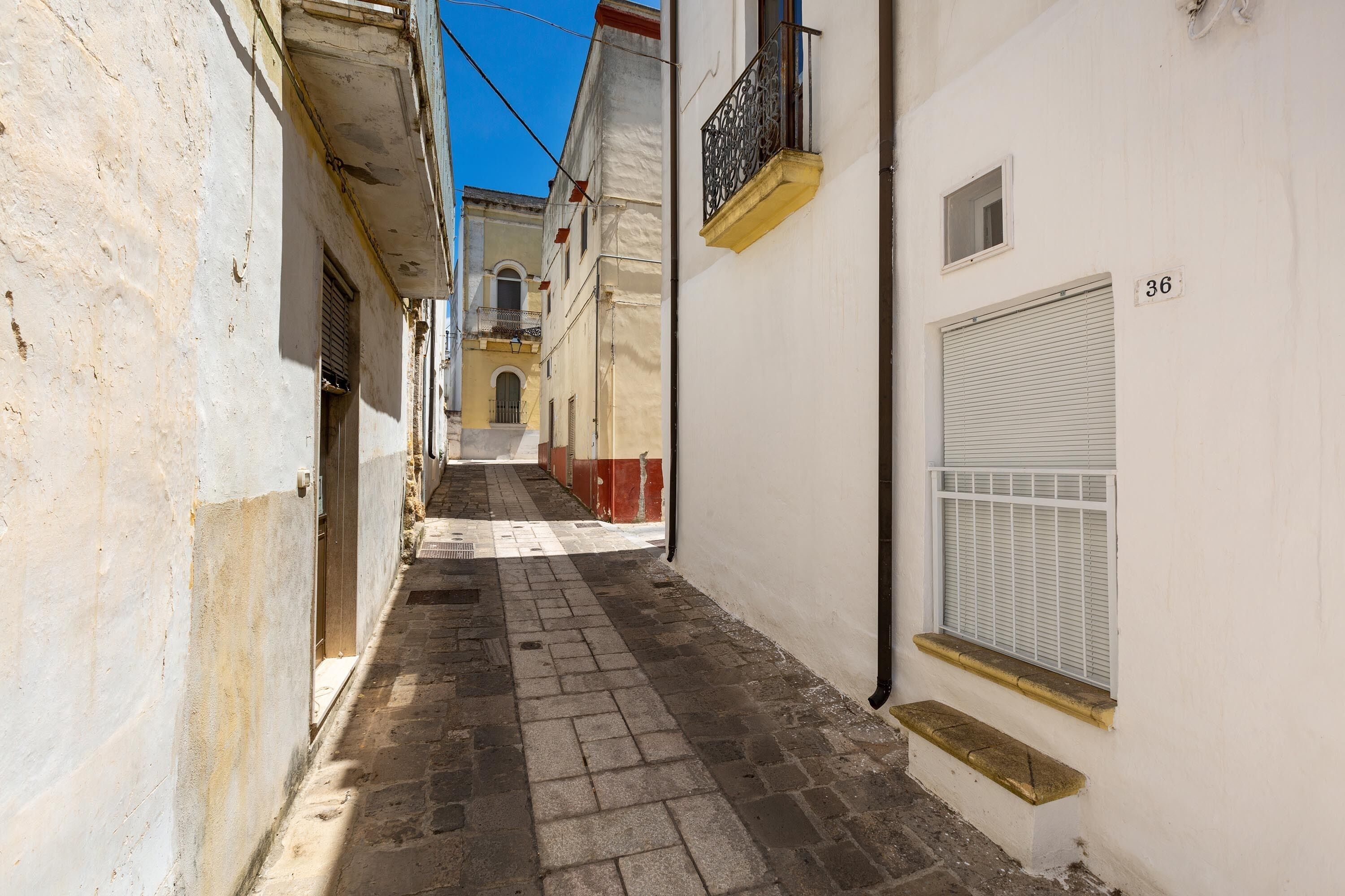Une ruelle étroite, avec un chemin pavé, des murs blancs et une fenêtre ornée de volets.