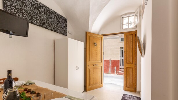A dining area with a table set for two, a bottle of olive oil, and a pitcher of water. There is a wooden door leading to an outdoor area. - 3482 Vico dei Mille by Barbarhouse (Tuglie)
