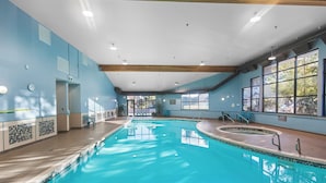 Una piscina interior con agua azul cristalina, terraza de madera y ventanas amplias.