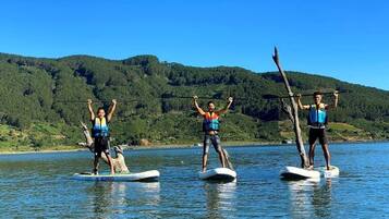 Three people stand-up paddleboarding on a calm lake with a forested hillside in the background.
