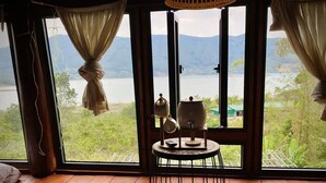 A room with a wooden floor, a round table with a kettle and teapot, and two round cushions. - Khu nghi duong Kala Campark (Bao Thuan)