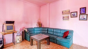 A living room with a teal sofa, a small wooden coffee table, a TV on a stand, and a vase with flowers. - Hotel O Toyo Homestay Syariah (Batam)