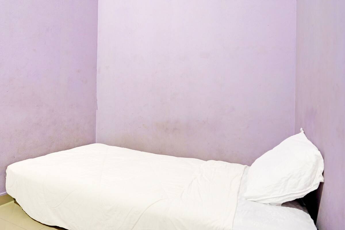 A small, single-bed room with a plain white mattress and a single white pillow.