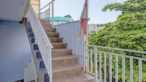 A set of beige carpeted stairs with white railings, leading to a balcony with a white railing and a red and white umbrella. - Hotel O Toyo Homestay Syariah (Batam)