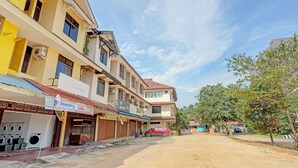 A multi-story building with a laundry service on the ground floor, a parked red car, and a dirt road in front. - Hotel O Toyo Homestay Syariah (Batam)